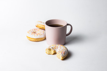 Pink Cup with coffee or tea and fresh tasty donuts, sweet multicolored decorative candy on a white background. Bakery concept, fresh pastries, delicious breakfast, fast food.