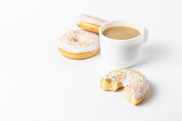 White Cup, coffee or tea with milk and fresh tasty donuts, sweet multicolored decorative candy on a white background. Bakery concept, fresh pastries, delicious breakfast, fast food.