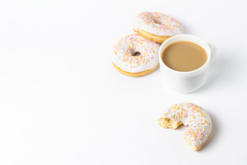 White Cup, coffee or tea with milk and fresh tasty donuts, sweet multicolored decorative candy on a white background. Bakery concept, fresh pastries, delicious breakfast, fast food.