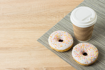 Delicious, sweet, fresh donuts and a paper cup with coffee or tea on a wooden background. Breakfast concept, fast food, coffee shop, bakery.