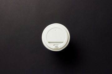 Paper transfer cup with a plastic lid, coffee or tea on a black background. Concept of breakfast, fast food, coffee shop, bakery, lunch. Flat lay, top view.