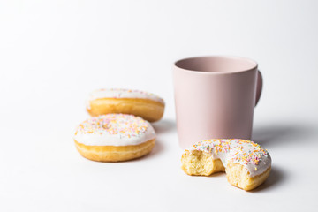 Pink Cup with coffee or tea and fresh tasty donuts, sweet multicolored decorative candy on a white background. Bakery concept, fresh pastries, delicious breakfast, fast food.