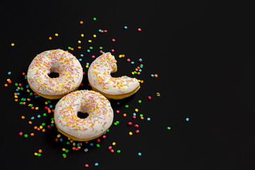 Delicious, sweet, fresh donuts and multicolored decorative candies on a black background. Breakfast concept, fast food, coffee shop, bakery.