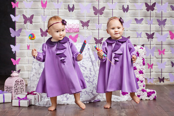 One-year-old twins on the birthday. Cute twin sisters celebrating their 1th birthday. Little twins girl dancing and holding colorful candies