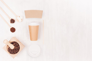 Coffee shop template for branding identity - brown paper cup with blank label, cap, mortar with coffee beans on white wood board, top view, copy space.