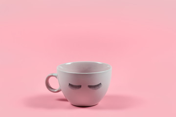 Cute pink coffee or tea mug with false lashes on a pink background. Morning energy. Female cute background.
