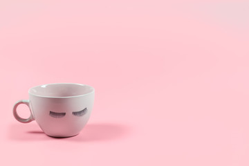 Cute pink coffee or tea mug with false lashes on a pink background with copy space. Morning energy. Female cute background.