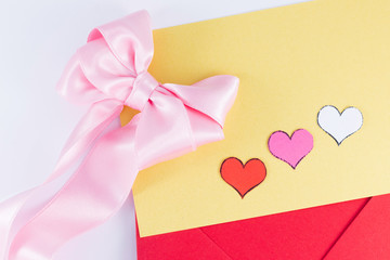 Red triangle envelope opened with yellow letter inside, three hearts pink bow near Valentine's day or festive concept Letter or invitation inside Minimalist concept Copy Space and template