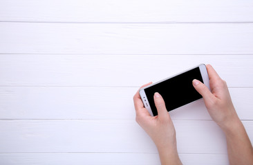 Female hands holding mobile phone with blank screen on white wooden background