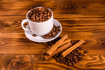 White cup filled with coffee beans and cinnamon sticks on wooden table