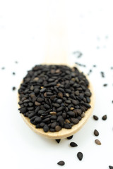 Black sesame on wooden spoon isolated on white background.