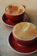 Two coffee cup, one latte and one mocha in red cup on rustic wooden table.