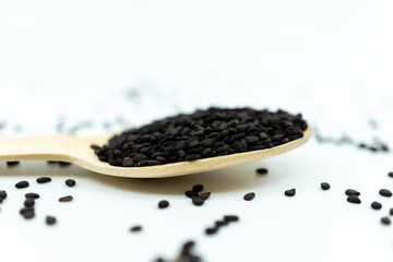 Black sesame on wooden spoon isolated on white background.