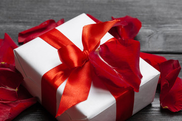 Gift box and rose petal on wooden background.