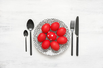 Red Easter eggs in plate with silverware