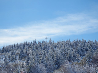 Cruz en lo ato de una montaña cubierta de arboles nevados