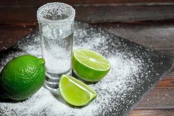 Tequila silver shots with lime slices and salt on wooden board