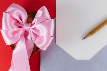 Silver open envelope with white blank letter Wooden pencil Red box with pink big bow on it Red background Letter or invitation Minimalist concept Copy Space and template