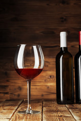 Glass and bottle with delicious red wine on table against wooden background