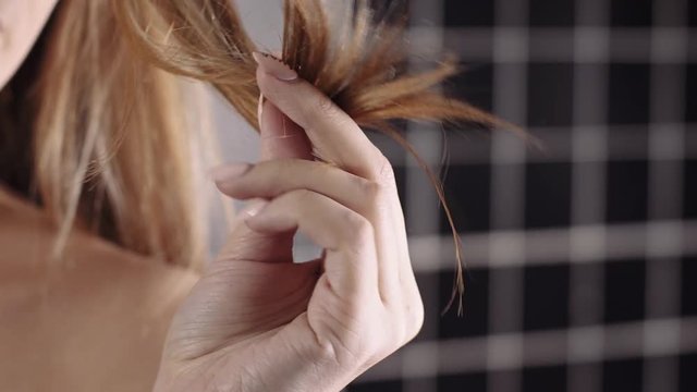 Woman holds her dry brittle hair in a hand, hair care, shampoo and cosmetics for strong hair, brittle tips
