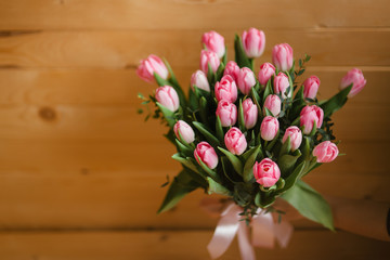 A bouquet of pink tulips in woman's hands. Woden background