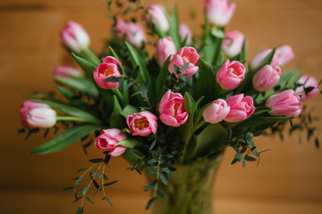A bouquet of pink tulips in a beautiful crystal vase on wooden background. Spring