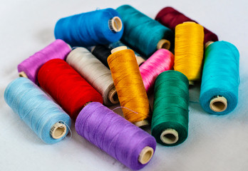 many bright color thread spools on white fabric - image