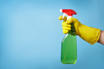 Hand in protective glove with house-cleaning spray isolated on blue background.