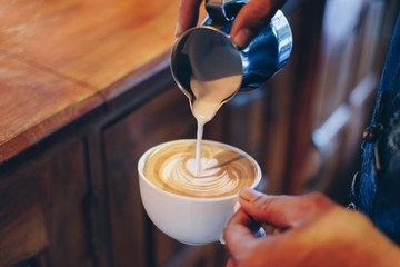 Hand barista pouring milk on coffee latte flower shape in cup