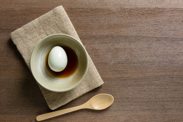 top view of boiled egg with soy sauce in a ceramic bowl on wooden table, copy space for text. cheap nutrition source concept.