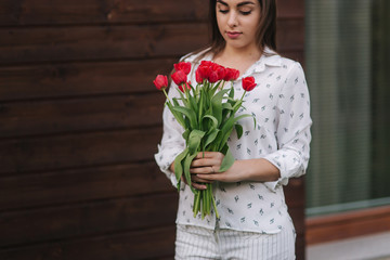 Beautiful girl with bouquet of red flowers stand by the house. Wooden background