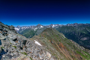 Mountain summit Dombai-Ulgen. In the background are glaciers and peaks of the Main Caucasus Range against the background of a piercing blue sky.