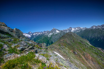 Fototapeta na wymiar Mountain summit Dombai-Ulgen. In the background are glaciers and peaks of the Main Caucasus Range against the background of a piercing blue sky.