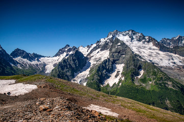 Fototapeta na wymiar Mountain summit Dombai-Ulgen. In the background are glaciers and peaks of the Main Caucasus Range against the background of a piercing blue sky.