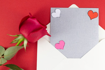 A fresh red rose big bud and petals with green leaves near white triangle envelope and empty silver letter and valentines Red background Invitation Minimalist concept Copy Space and template