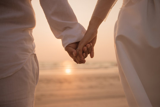 Romantic couple holding hand against the sea at sunset.
