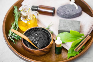 Skincare ingredients with charcoal mask, olive oil, herbal botanical essential oil bottle, natural soap, rosemary herb, holistic natural skincare and bodycare ingredients in wooden tray