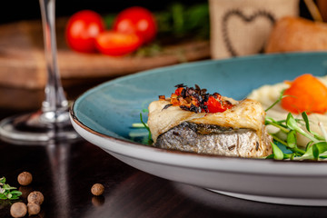 The concept of Italian cuisine. Baked Seabass Fish with Vegetables and Mashed Potatoes. A glass of white wine on the table. Servovika dishes in the restaurant. copy space