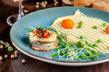 The concept of Italian cuisine. Baked Seabass Fish with Vegetables and Mashed Potatoes. A glass of white wine on the table. Servovika dishes in the restaurant. copy space