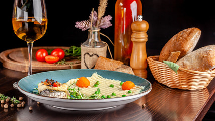 The concept of Italian cuisine. Baked Seabass Fish with Vegetables and Mashed Potatoes. A glass of white wine on the table. Servovika dishes in the restaurant. copy space