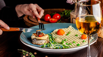 The concept of Italian cuisine. Baked Seabass Fish with Vegetables and Mashed Potatoes. A glass of white wine on the table. Servovika dishes in the restaurant. copy space