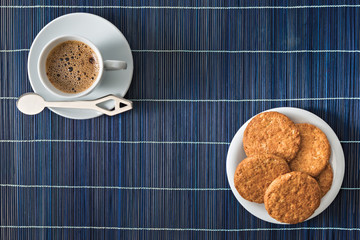 tazzina caffè e piattino biscotti con tovaglietta di stuoia bambù blu scatto da sopra concetto...