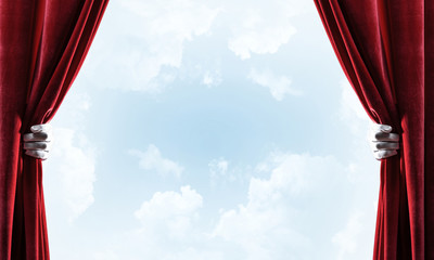 Cloudy landscape behind red curtain and hand holding it