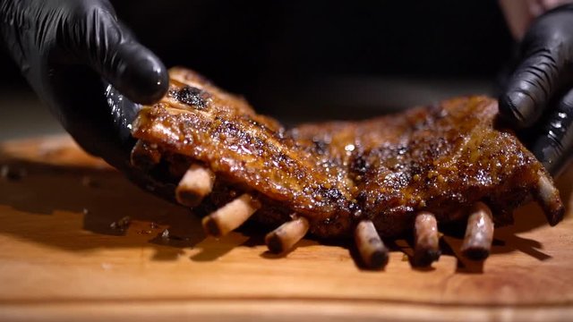 Closeup of hands in black rubber gloves holding cooked delicious lamb ribs