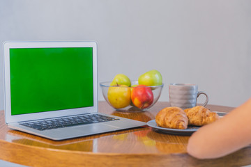 Cropped snapshot of feminine hands with disposable cups of coffee and croissants. Laptop and accessories on the table.Green screen