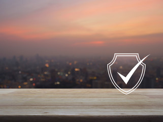 Fototapeta na wymiar Security shield with check mark flat icon on wooden table over blur of cityscape on warm light sundown, Technology internet cyber security and anti virus concept