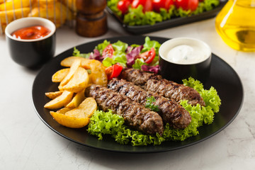 Traditional cevapcici served with baked potatoes. Stone background.