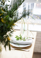 Beautiful springtime table setting with green leaves and mimosa branches, bright white table dinner decoration