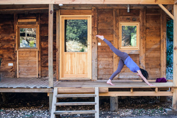 A woman practices yoga on the porch of an old wooden house.