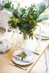 Beautiful springtime table setting with green leaves and mimosa branches, bright white table dinner decoration
